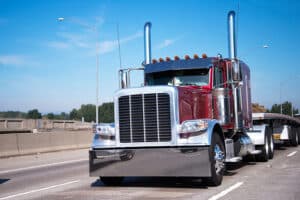 Classic big rig semi truck in dark red and flat bed semi trailer going to warehouse for loading cargo