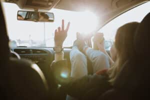 Woman is using V sign gesture inside of car at sunset