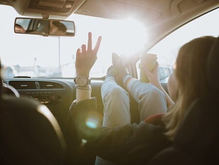 Woman is using V sign gesture inside of car at sunset